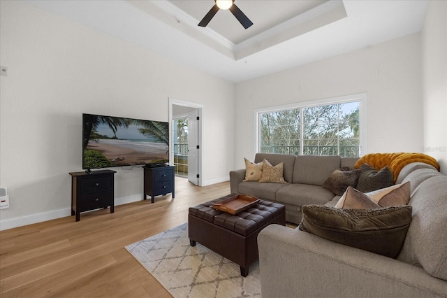 living room with light wood-type flooring, a tray ceiling, and ceiling fan