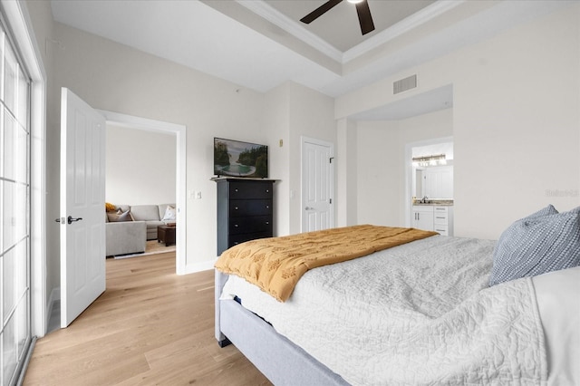 bedroom with ensuite bath, ornamental molding, a raised ceiling, ceiling fan, and light hardwood / wood-style floors