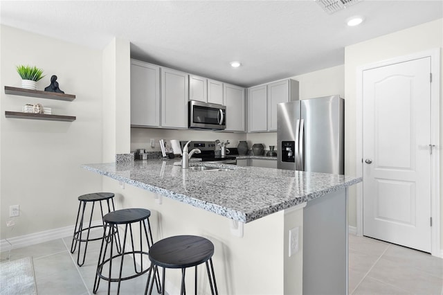 kitchen featuring kitchen peninsula, appliances with stainless steel finishes, light stone counters, sink, and light tile patterned floors