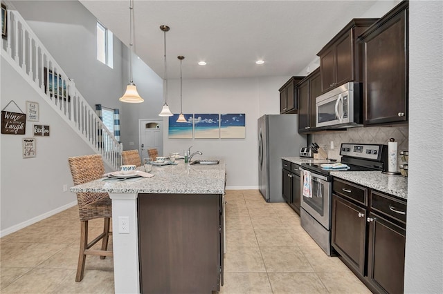 kitchen featuring appliances with stainless steel finishes, light tile patterned floors, hanging light fixtures, a breakfast bar area, and an island with sink