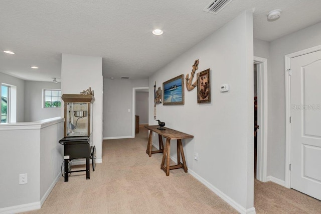 corridor with light carpet and a textured ceiling