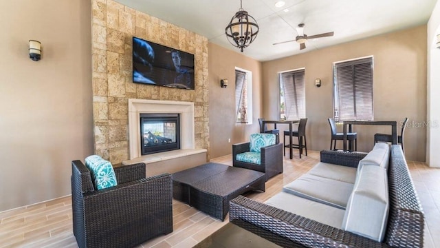 living room featuring an outdoor stone fireplace and ceiling fan with notable chandelier