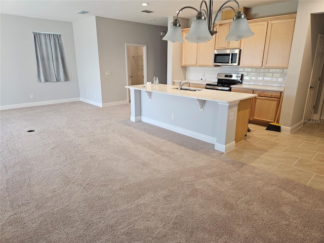 kitchen featuring light brown cabinets, stainless steel appliances, a center island with sink, and backsplash