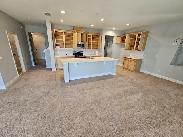 kitchen featuring a breakfast bar, sink, light carpet, appliances with stainless steel finishes, and a kitchen island with sink