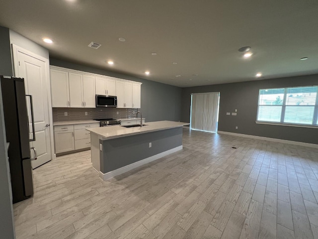 4535 Gliding Wave St, Winter Garden, FL 34787 - kitchen with appliances with stainless steel finishes, white cabinetry, backsplash, a center island with sink, and light wood-type flooring