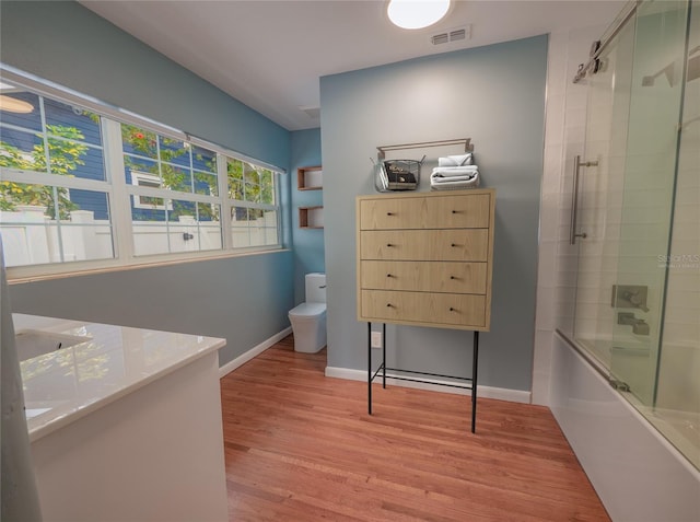 bathroom featuring hardwood / wood-style floors, bath / shower combo with glass door, and toilet