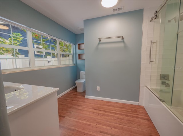 full bathroom with hardwood / wood-style flooring, vanity, toilet, and bath / shower combo with glass door