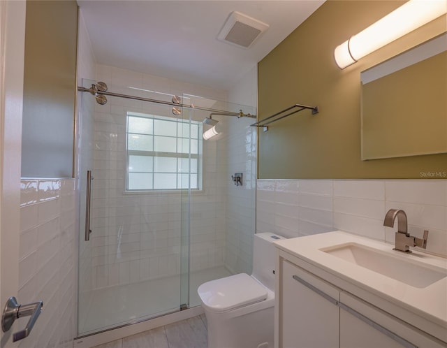 bathroom with vanity, a shower with door, toilet, and tile walls