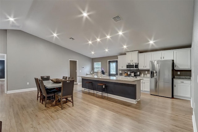 kitchen featuring white cabinetry, an island with sink, vaulted ceiling, decorative backsplash, and appliances with stainless steel finishes