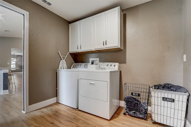 clothes washing area featuring cabinets, light hardwood / wood-style flooring, and washer and dryer