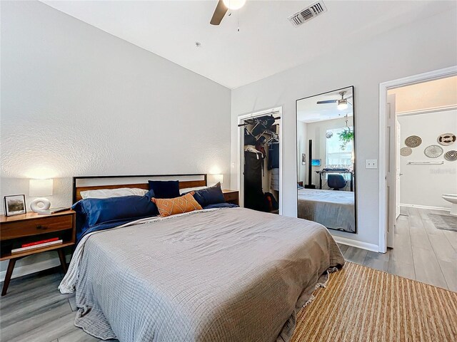 bedroom with a walk in closet, vaulted ceiling, light hardwood / wood-style flooring, a closet, and ceiling fan