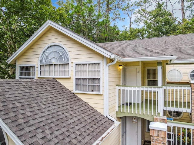 exterior space featuring a downspout, a shingled roof, and gutters