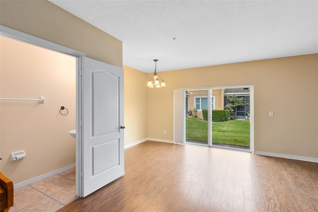 unfurnished room featuring a notable chandelier, light hardwood / wood-style floors, and a textured ceiling