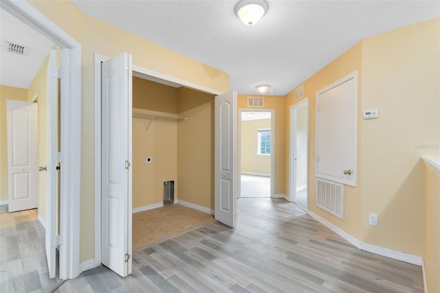 hall with light wood-type flooring and a textured ceiling