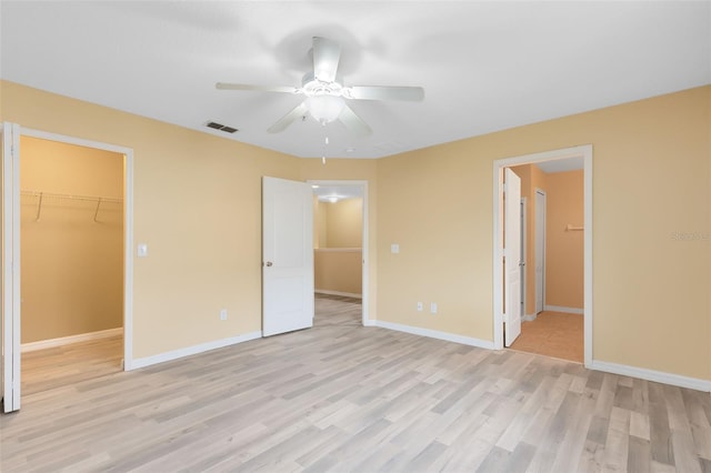 unfurnished bedroom with ensuite bathroom, ceiling fan, a spacious closet, light hardwood / wood-style flooring, and a closet