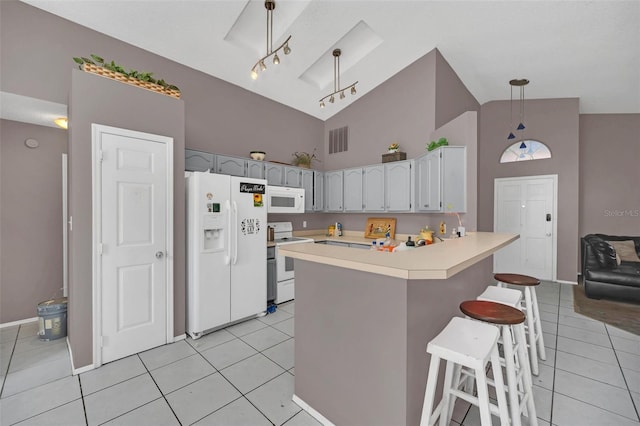 kitchen with a breakfast bar, white appliances, light tile patterned floors, high vaulted ceiling, and hanging light fixtures