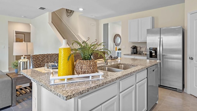 kitchen featuring sink, light stone counters, a center island with sink, white cabinets, and appliances with stainless steel finishes