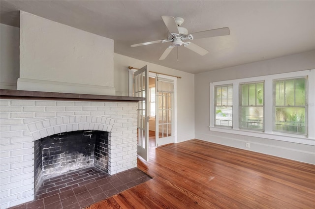 unfurnished living room featuring a brick fireplace, dark hardwood / wood-style floors, and ceiling fan