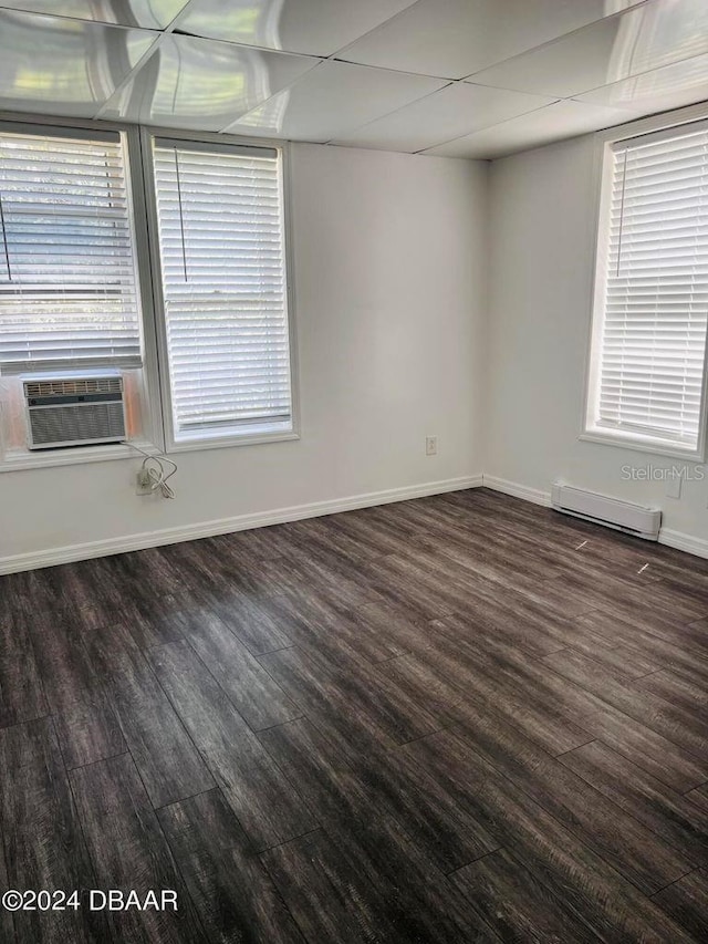 spare room featuring a healthy amount of sunlight, a baseboard heating unit, dark hardwood / wood-style floors, and a drop ceiling