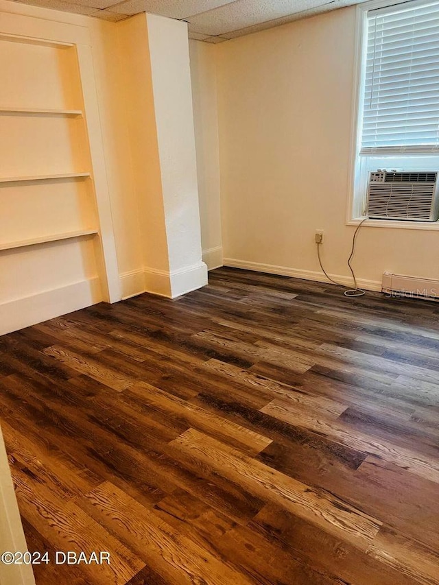 empty room with built in shelves, a drop ceiling, and dark hardwood / wood-style flooring