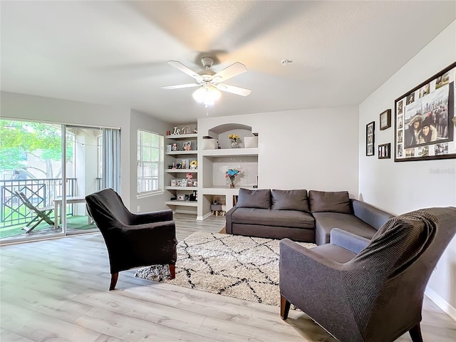 living room featuring built in shelves, light hardwood / wood-style floors, and ceiling fan