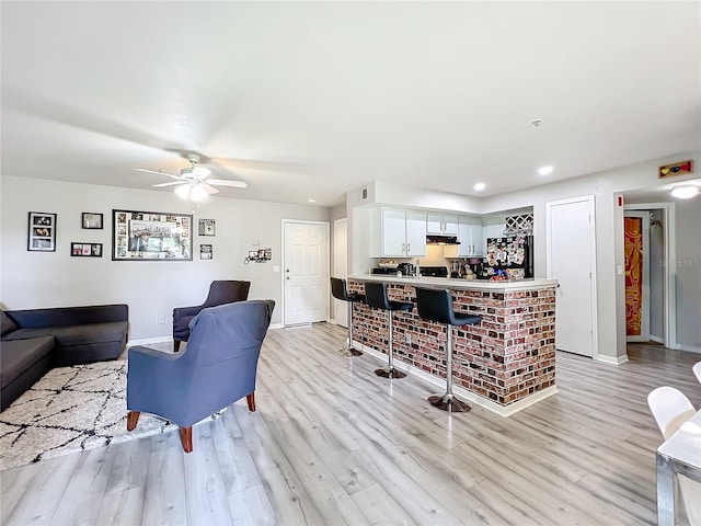 living room featuring bar, ceiling fan, and light wood-type flooring