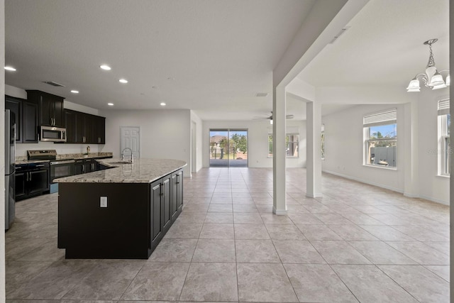 kitchen with a center island with sink, sink, light stone countertops, appliances with stainless steel finishes, and decorative light fixtures