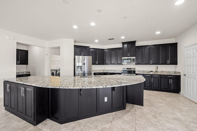 kitchen with light stone countertops, appliances with stainless steel finishes, independent washer and dryer, and a large island