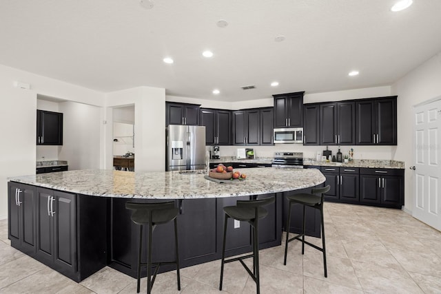 kitchen with a breakfast bar, appliances with stainless steel finishes, light stone countertops, and a large island with sink