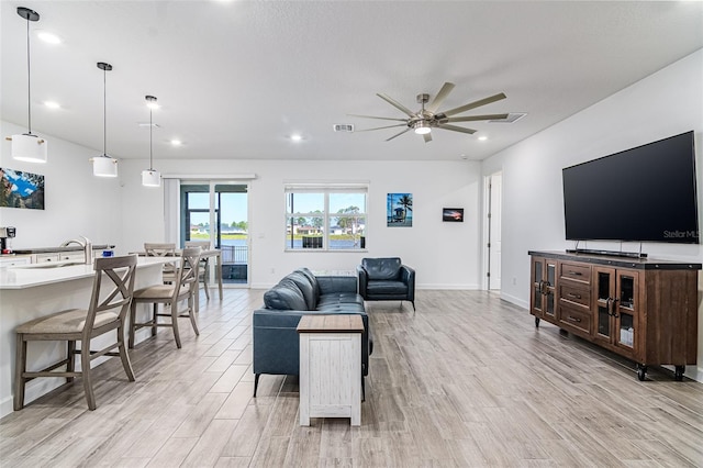 living room featuring ceiling fan, sink, and light wood-type flooring