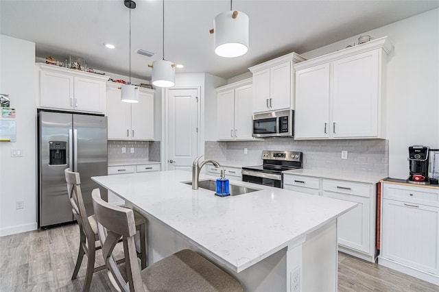 kitchen with sink, stainless steel appliances, hanging light fixtures, and an island with sink