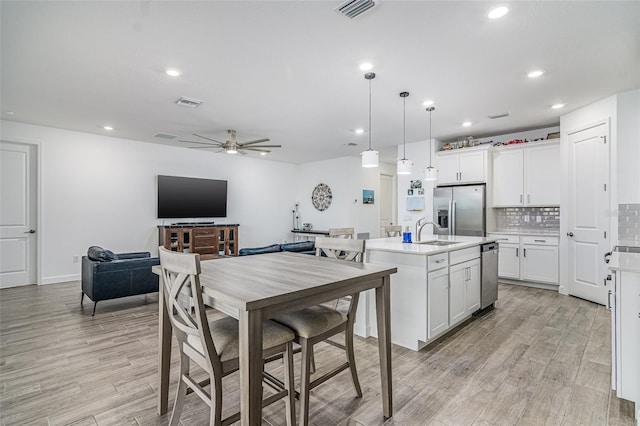 kitchen with pendant lighting, white cabinetry, an island with sink, stainless steel fridge, and light hardwood / wood-style flooring