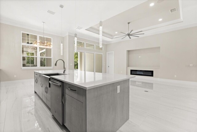 kitchen with modern cabinets, stainless steel dishwasher, a center island with sink, a sink, and a tray ceiling