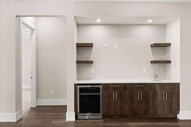 bar featuring a sink, beverage cooler, dark wood finished floors, indoor wet bar, and baseboards