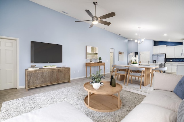 living room with ceiling fan with notable chandelier, light hardwood / wood-style flooring, and high vaulted ceiling