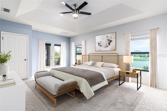 bedroom featuring a water view, access to exterior, a raised ceiling, and multiple windows