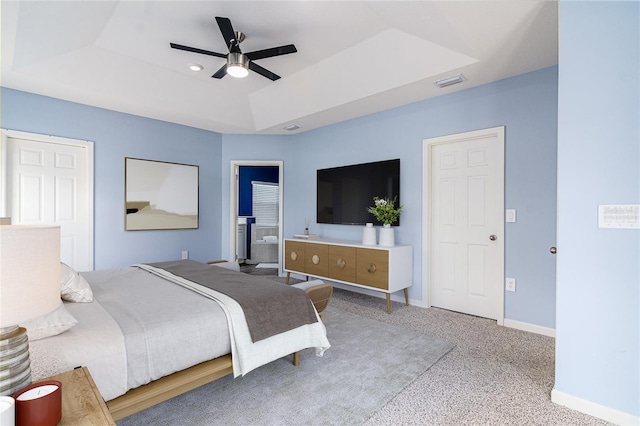 carpeted bedroom featuring ceiling fan, a tray ceiling, and ensuite bath