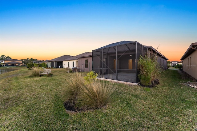 back house at dusk with a patio area, a lawn, and glass enclosure