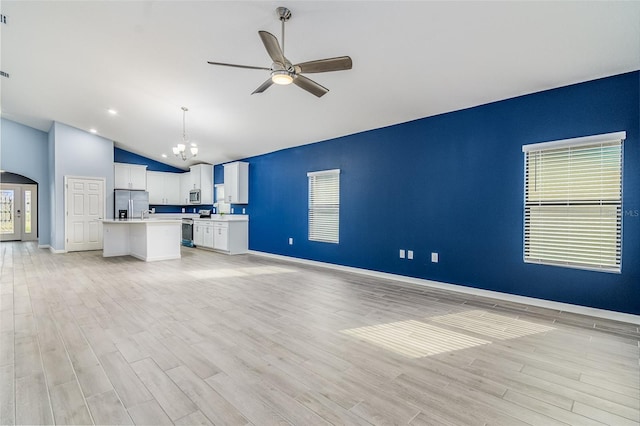 unfurnished living room with ceiling fan with notable chandelier, vaulted ceiling, and light wood-type flooring