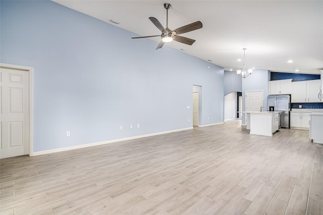 unfurnished living room with high vaulted ceiling, ceiling fan with notable chandelier, and light hardwood / wood-style floors