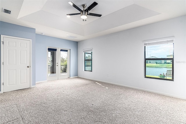 carpeted empty room with a raised ceiling, plenty of natural light, ceiling fan, and a water view