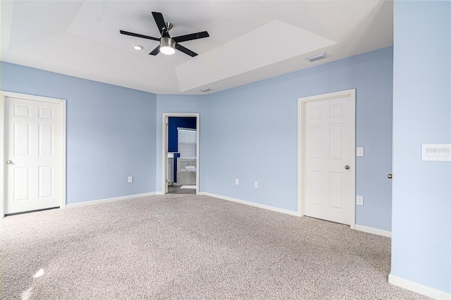 unfurnished bedroom featuring ceiling fan, ensuite bath, a raised ceiling, and carpet floors