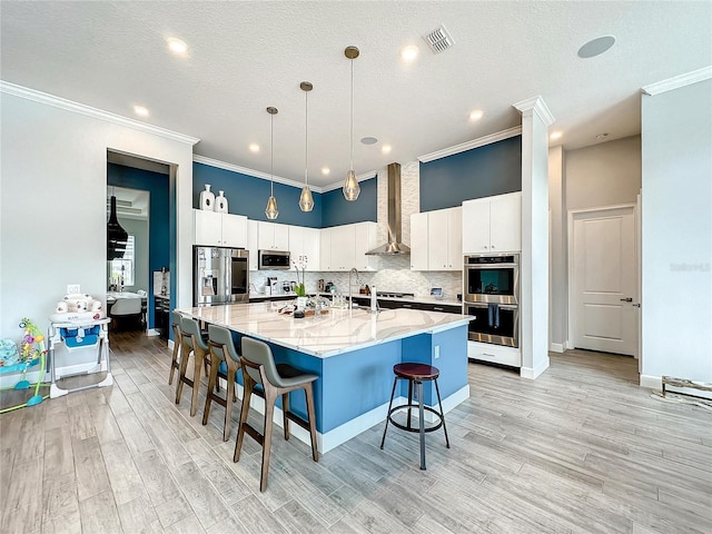 kitchen featuring white cabinetry, stainless steel appliances, wall chimney range hood, decorative backsplash, and a breakfast bar