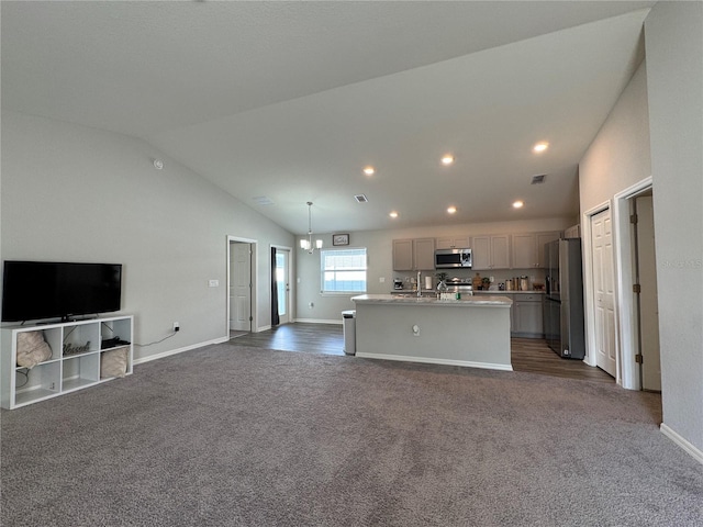 kitchen featuring pendant lighting, dark carpet, a center island with sink, vaulted ceiling, and appliances with stainless steel finishes