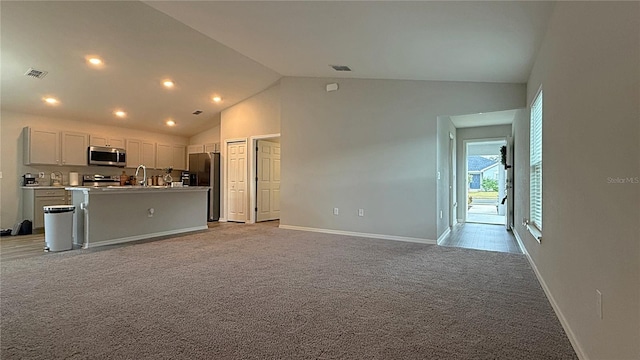 kitchen featuring sink, stainless steel appliances, light carpet, high vaulted ceiling, and a kitchen island with sink