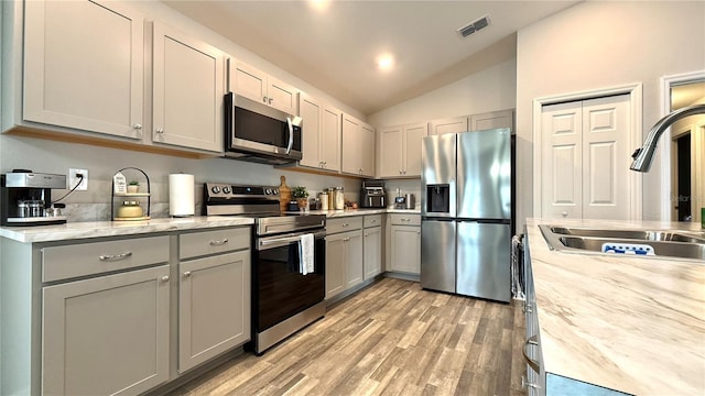 kitchen featuring appliances with stainless steel finishes, gray cabinets, lofted ceiling, and sink