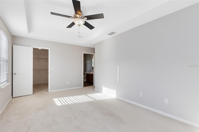 unfurnished bedroom with a walk in closet, ensuite bath, a tray ceiling, ceiling fan, and a closet