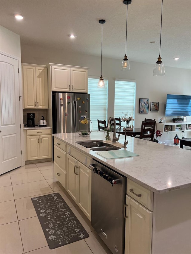 kitchen featuring decorative light fixtures, light stone counters, stainless steel appliances, and a kitchen island with sink