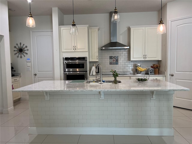 kitchen featuring a kitchen bar, decorative light fixtures, light stone countertops, and wall chimney range hood