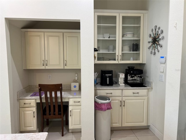 bar featuring tasteful backsplash, cream cabinets, light tile patterned floors, and built in desk